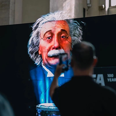 Großes digitales Porträt von Albert Einstein auf Leinwand, im Vordergrund Person fotografiert mit Smartphone, Ausstellung 2024