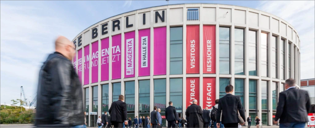 Menschen strömen zum Messegebäude mit großen Magenta- und roten IFA-Bannern am Eingang in Berlin